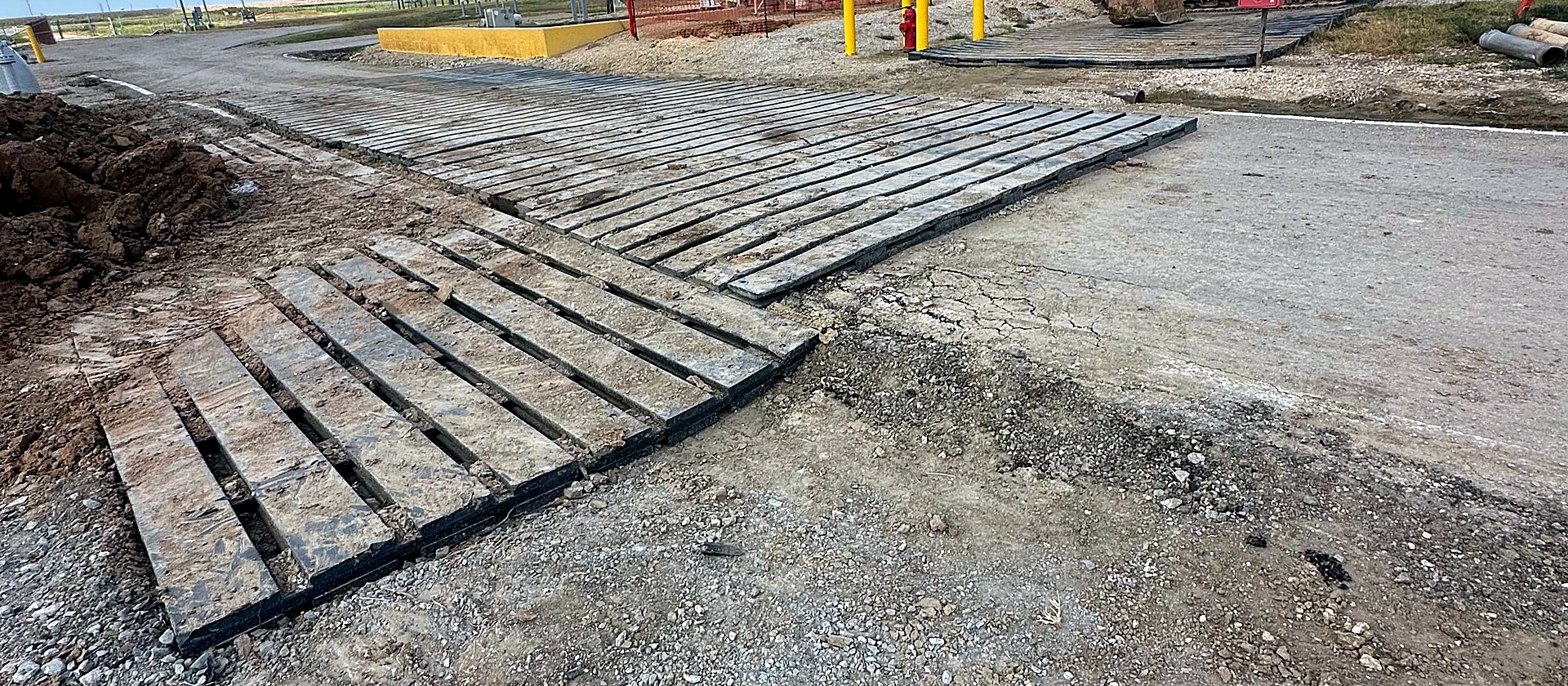 Recycled HDPE mats staged at a plant site with an excavator working beyond